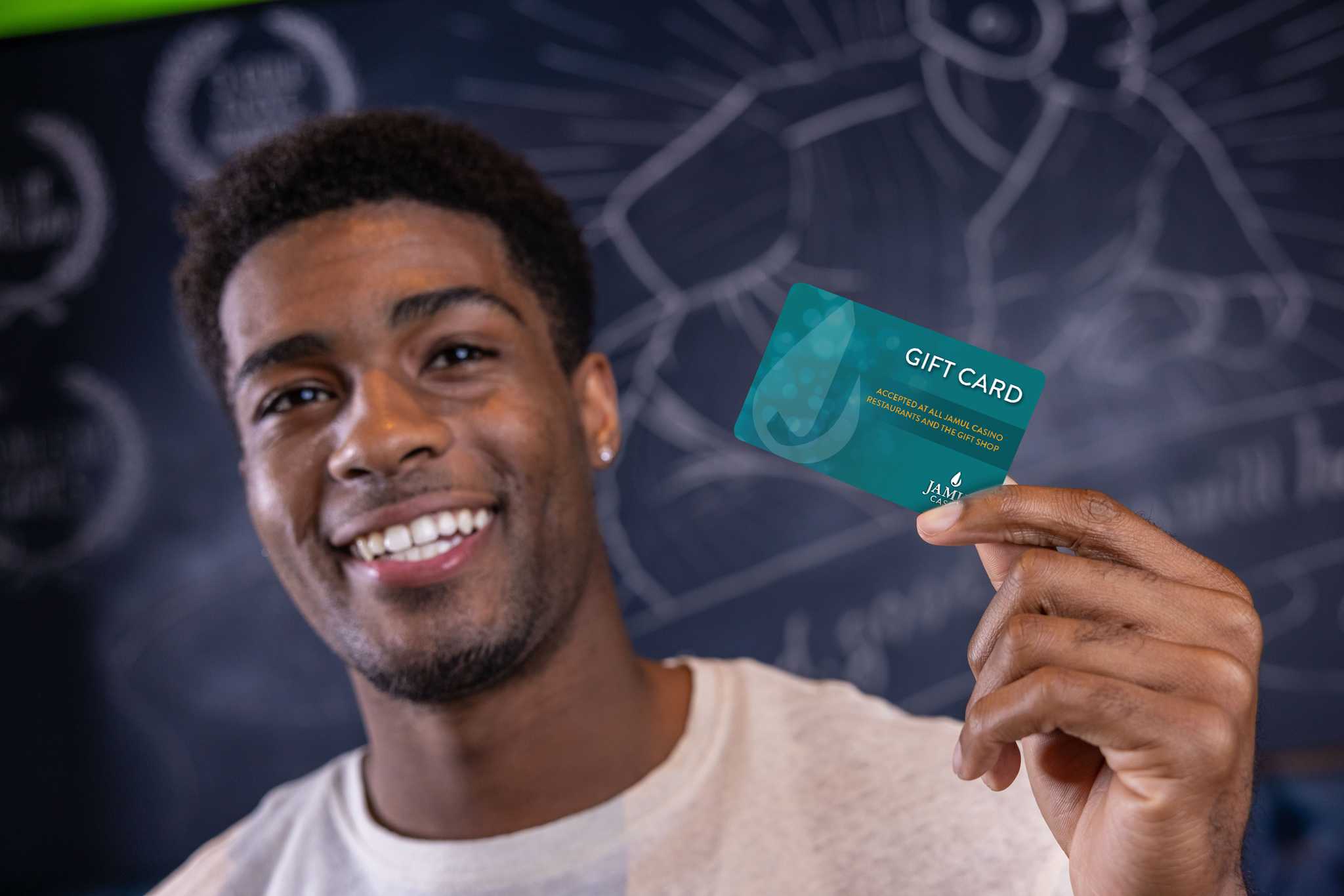 A young man smiling and holding up the Jamul Casino Resort gift card.